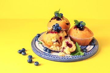 Plate with tasty blueberry muffins on color background