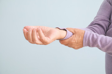 Obraz premium Senior woman suffering from pain in wrist against light background