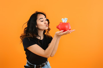 Happy Asian woman with piggy bank on color background