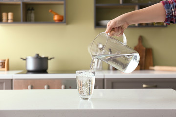 Woman pouring fresh water from jug into glass on table