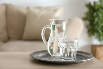 Glass and jug of fresh water on table in room