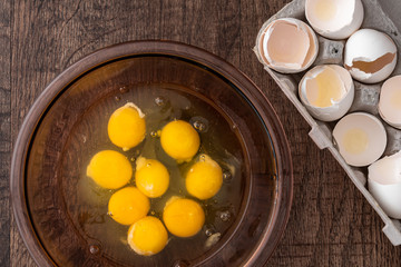 Egg shells in cardboard egg carton, raw eggs in glass bowl, on a wood table