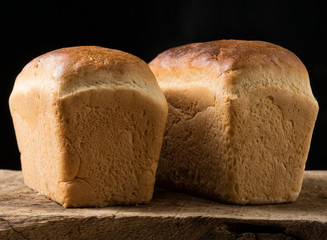Two loaves of white bread on an oak board