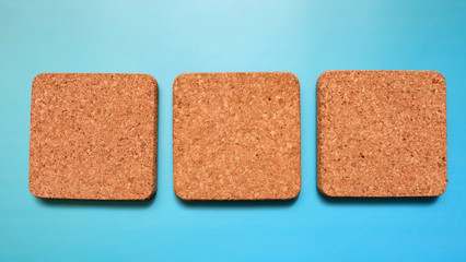 3 square cork tiles arrange in a row next to each other, with a blue background.