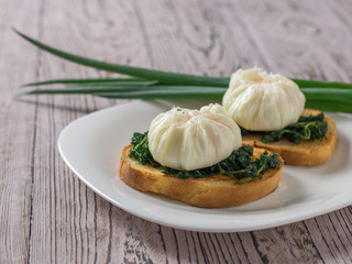 Two poached eggs with bread and green onions on a wooden table.