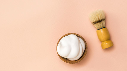 Shaving brush and shaving foam in a wooden bowl on a coral background.
