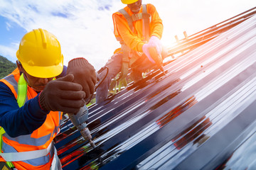 Roofer worker using air or pneumatic nail gun and installing metal sheet on top of the new roof.