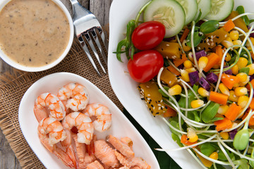 Fresh salad plate with shrimp, salmon, tomato and mixed greens  on wooden background .