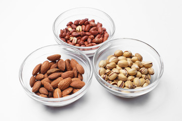 peanuts, almonds and pistachios in bowls on white background