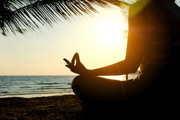 Silhouette of a woman doing meditation on the beach of the sea during the morning hours.