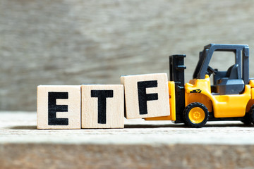Toy forklift hold letter block f to complete word ETF (abbreviation of Exchange Traded Fund) on wood background