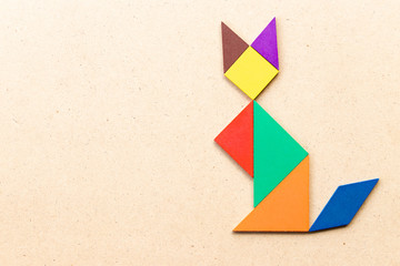 Color tangram puzzle in sitting cat shape on wood background