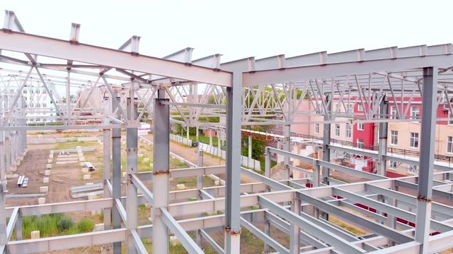 Aerial flight rise above the metal frames of the building under construction. Metal piles streak in the shot. Taken by drone