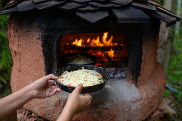 Hands of woman holding pizza pan put into charcoal oven