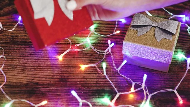 hand grabbing a Christmas gift box next to another surrounded by festive golden fairy lights