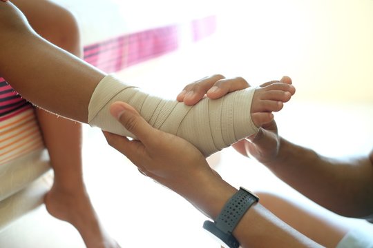 Injured Kid Ankle. Father Rewinds Kid’s Leg With An Elastic Ankle Support.