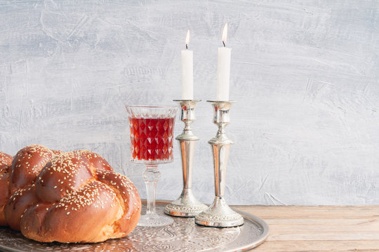 Shabbat or Sabbath kiddush ceremony composition with a traditional sweet fresh loaf of challah bread, glass of red kosher wine and candles on a vintage wood table with copy space