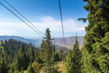 Summer mountain landscape high in the mountains. Tall trees of Christmas trees, ski lift at the ski base.