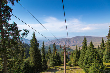 Summer mountain landscape high in the mountains. Tall trees of Christmas trees, ski lift at the ski base.