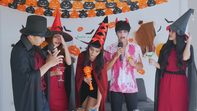 4K Gang young Asian in costume witch, wizard with celebrate Halloween party for sing a song and drink, dessert in the room. Group teen Thai with celebrate Halloween. Concept party Halloween at home.