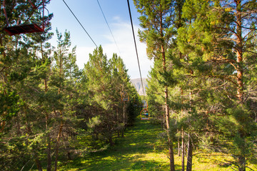 Obraz premium Summer mountain landscape high in the mountains. Tall trees of Christmas trees, ski lift at the ski base.