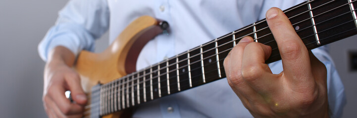 Male arms holding and playing classic shape wooden electric guitar closeup. Six stringed learning...