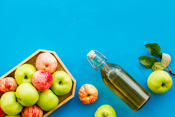 Apple cider in bottle near tray with fruits on blue background top view copy space
