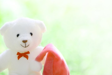 Closeup one white teddy bear with red bow and red Christmas cap on blur green and white background have copy space for put text