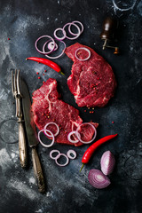 Two Raw beef steak with spices, onions and chili on dark slate or concrete background. Top view