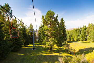 Summer mountain landscape high in the mountains. Tall trees of Christmas trees, ski lift at the ski...
