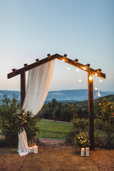Wooden wedding arch with white cloth and light bulbs outdoors with amazing mountain view on...