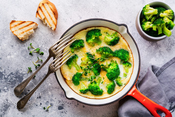 Omelette with broccoli and green young onions on red cast iron pan on old gray concrete background. Top view.