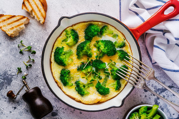 Omelette with broccoli and green young onions on red cast iron pan on old gray concrete background. Top view.