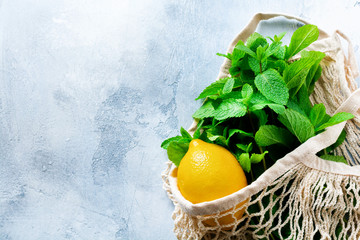Mint leaves, fresh lemon and honey lying holding mesh shopping cotton bag on old gray concrete background. Top view. Zero waste Concept.