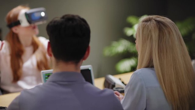 Camera moving from female tester in VR goggles to talking developers during virtual reality test in office