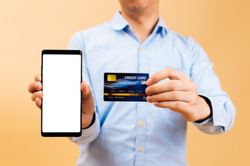 Crop man in formal shirt carrying smartphone with empty screen and credit card over yellow background