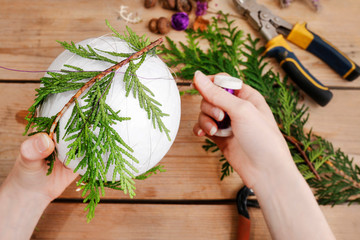 Woman shows how to make Christmas ball with styrofoam sphere and thuja twigs