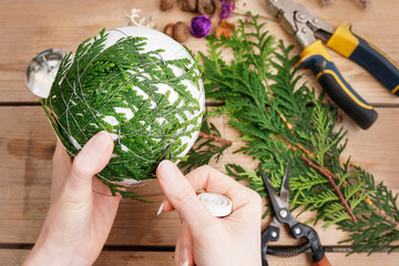 Woman shows how to make Christmas ball with styrofoam sphere and thuja twigs