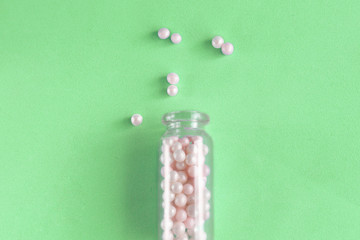 Homeopathy pills in glass bottle on green background, top view. Homeopathic medicine globules - herbal remedy alternative medication.