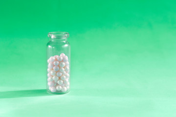 Homeopathy pills in teaspoon on green background. Homeopathic medicine globules - herbal remedy alternative medication.