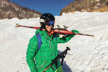 Young man holding ski, he looking away and smiling.