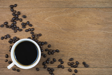 Coffee cup and coffee beans on wooden table background. Top view with copy space.