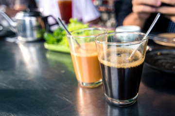 Black coffee and milk tea in transparent glass on stainless table in breakfast restaurant.