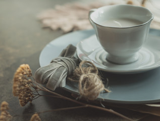 Autumn background with a cup-candles, dried flowers and macrame feather. Cozy background in gray colors.