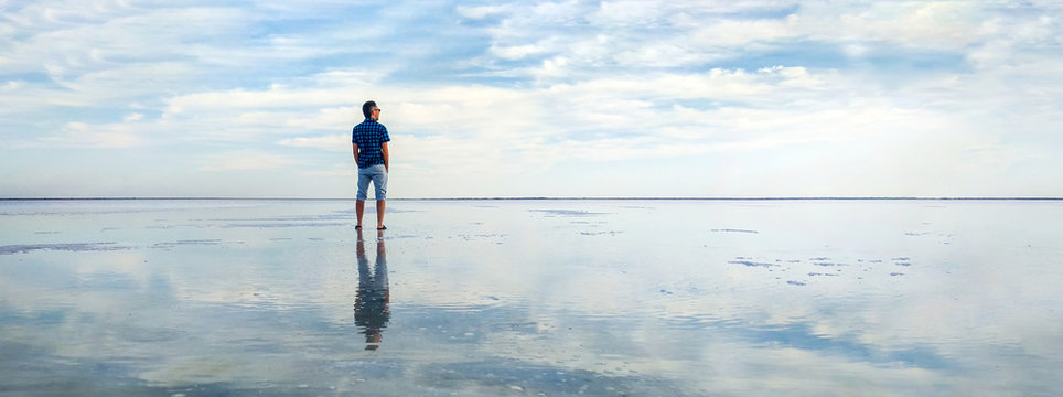 Man In The Water At Sea. Concept Of A Happy Holiday And Freedom. Tourist Looking At The Horizon Line. Beautiful Panorama Of The Salt Lake With The Reflection Of White Clouds In The Ode.