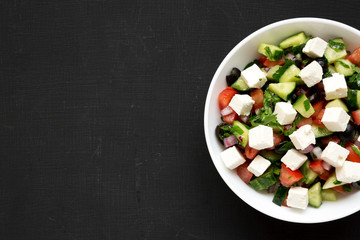 Homemade Shepherd's salad with cucumbers, feta and parsley in a white bowl over black background, top view. From above, overhead, flat lay. Space for text.