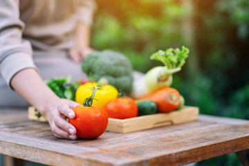 A woman holding and picking a fresh mixed vegetables from a wooden tray on the table