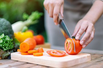 Closeup image of a woman cutting and chopping tomato by knife on wooden board