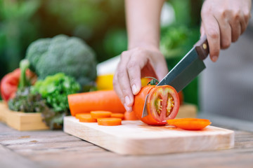 Closeup image of a woman cutting and chopping tomato by knife on wooden board