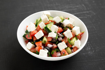 Homemade Shepherd's salad with parsley, cucumbers and feta in a white bowl over black surface, side view. Close-up.